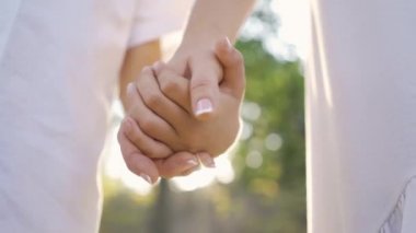 Parkta ya da ormanda duran beyaz giyimli iki kişinin yakın elleri. El ele tutuşuyor. Boş zaman açık havada, iyi ilişkiler.