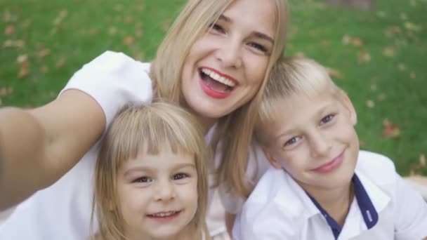 Mujer caucásica joven y dos niños tomando selfie en el parque. Madre con hijos riéndose. Mamá hablando con sus hijos. Familia divirtiéndose al aire libre . — Vídeos de Stock