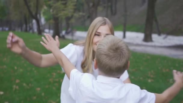 Tillbaka syn på blond pojke som kör mot sin mor. Attraktiv ung kvinna kramar sin son och leende. Lycklig familj umgås tillsammans i parken. Slow motion. — Stockvideo