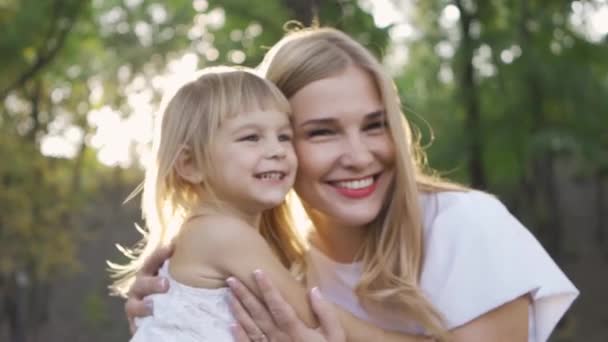 Hermosa mujer rubia con una niña linda mirando a la cámara y sonriendo. Ocio al aire libre. Familia feliz. Un padre. Maternidad, paternidad, infancia feliz . — Vídeo de stock