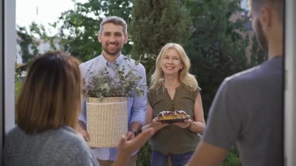 Back view of married couple meeting guests standing at the doors. Friendly neighbours visiting their friends bringing cake and presents. Concept of friendship, good relationship — Stock Video