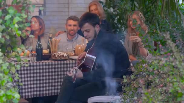 En grupp kaukasiska personer lyssnar på den unge mannen som spelar gitarr. Gamla vänner spenderar kväll tillsammans. — Stockvideo