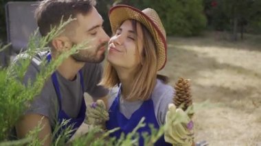 Bahçede dururken mavi üniformalı çekici beyaz kadın ve yakışıklı bir adamın konuşması ve öpüşmesi portresi. Elinde çam kozalağı olan kız. Bahçede erkek ve kadın işçiler