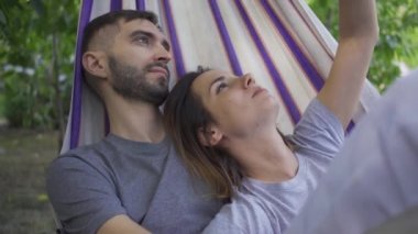 Mutlu genç beyaz adam ve kadın bahçede hamakta yatarken birlikte dinleniyor. Dışarıda sevgi dolu bir çift. Yaz tatili
