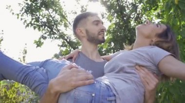 Genç adam karısını kollarına adamış. Yaz parkında eğlenen mutlu çift. Aktif yaşam tarzı, boş zaman açık havada