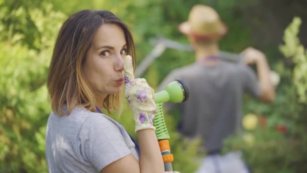 Eine glückliche Frau und ein Mann arbeiten im Garten. Mädchen spritzt aus dem Schlauch auf ihren Mann. fröhliche, glückliche Familie. — Stockvideo