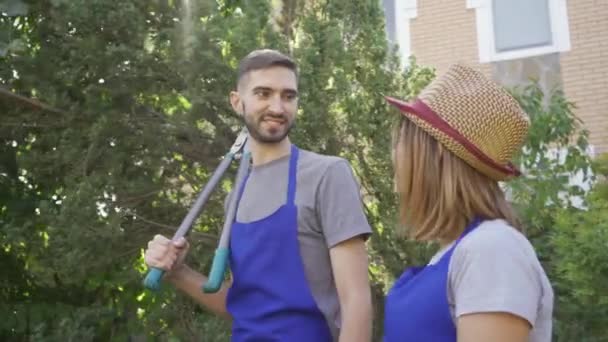Arbeiterinnen und Arbeiter in blauer Uniform spazieren durch den Garten und unterhalten sich. Jungbauer verliebt sich in seinen Arbeitskollegen. Paar ruht sich nach harter Arbeit aus — Stockvideo