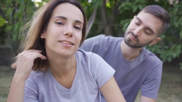 Retrato de una joven familia sentada en el jardín de verano. Feliz familia joven descansando al aire libre. Concepto de felicidad, relación, ternura — Vídeos de Stock