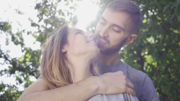 Портрет молодого чоловіка, який обіймає свою дівчину під сонячним світлом в літньому саду. Щаслива молода сім'я відпочиває на відкритому повітрі. Поняття щастя, відносин, ніжності — стокове відео