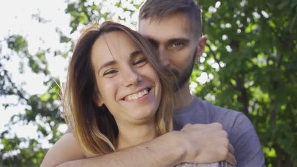 Портрет щасливий молодий чоловік обіймає свою дівчину на сонячному світлі в літньому саду. Щаслива молода сім'я відпочиває на відкритому повітрі. Поняття щастя, відносин, ніжності — стокове відео