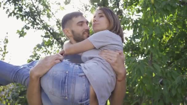 Ung man snurrar runt och håller sin hustru i armar. Lyckligt par ha kul i sommar parken. Aktiv livsstil, fritid utomhus — Stockvideo
