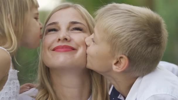 Närbild av liten flicka och pojke kysser kinder av mamma. Lycklig familj i Park. Fritid utomhus. Moderskap, föräldraskap, barndom. — Stockvideo