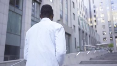 Beyaz gömlekli Afro-Amerikan adamın arka görünümü büyük modern iş merkezine doğru yürüyor. Erkek işadamı veya yönetici ofise gidiyor