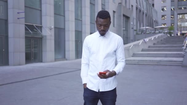 Hombre afroamericano guapo con camisa blanca hablando por teléfono celular rojo parado en la calle de la ciudad. Hombre de negocios o gerente en el edificio moderno — Vídeos de Stock