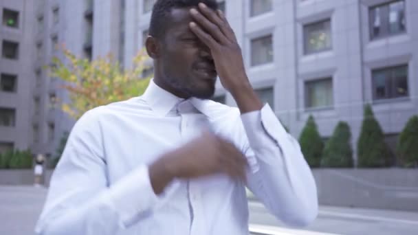 Bonito afro-americano de camisa branca segurando a cabeça com as mãos em pé na rua da cidade. Homem empresário ou gerente frustrado e desapontado — Vídeo de Stock