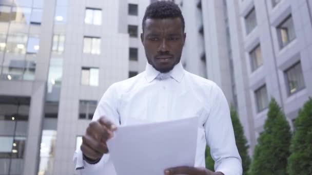 Close-up van Afro-Amerikaanse man in wit shirt lezen van documenten en gooi ze weg. Mannelijke zakenman of manager moe en gestrest. — Stockvideo
