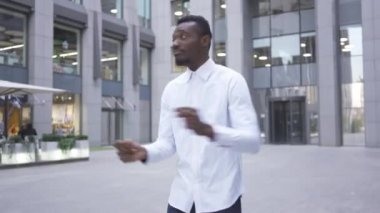 Kendine güvenen Afro-Amerikan adam beyaz gömlek dans ve şehir caddesinde modern iş merkezinin önünde şarkı. Erkek işadamı veya yönetici harika haber var.