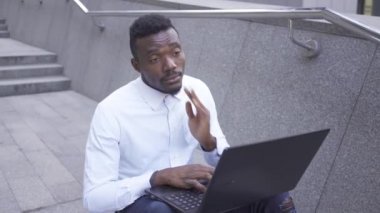 Beyaz gömlek li bitkin Afro-Amerikan adam esneme ve dizüstü bilgisayarda yazarak. Yorgun erkek işadamı veya yönetici uykuya dalmak için çalışıyor açık havada çalışıyor.