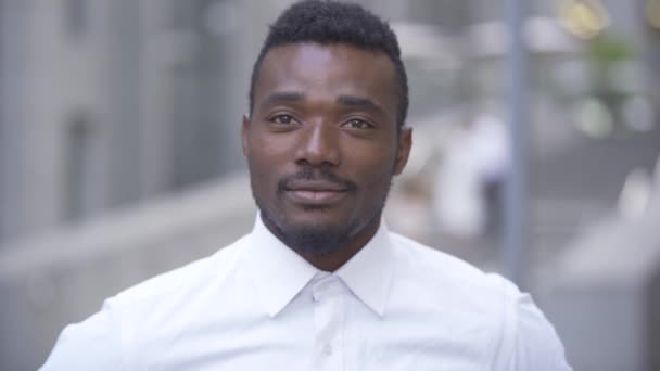 Yakışıklı gülümseyen Afro-Amerikan adamın yakın çekim portresi beyaz gömlekli şehir caddesinde dururken kameraya bakıyor. Erkek işadamı veya iş yerinde yönetici — Stok video