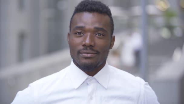 Close-up portret van knappe glimlachende Afro-Amerikaanse man in wit overhemd kijkend naar de camera terwijl hij op de straat van de stad staat. Mannelijke zakenman of manager aan het werk — Stockvideo