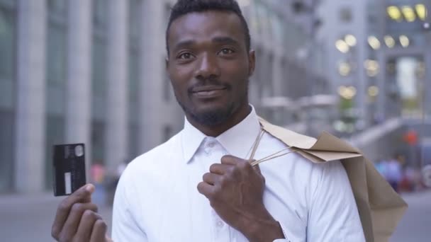 Rijke Afro-Amerikaanse man die op de straat van de stad staat en zijn bankkaart laat zien. Mannelijke zakenman of manager naar kantoor of naar huis na het winkelen. — Stockvideo