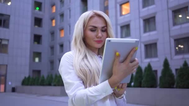 Portrait of blond caucasian woman in white jacket working with the tablet standing on the city street. Businesswoman or top manager at the modern business center — Αρχείο Βίντεο