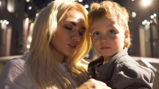 Närbild av attraktiv blond kvinna i vit skjorta som håller hennes lille pojke på händerna. Mor och son pratar på kvällen. Lady-Boss spenderar tid med sin unge. — Stockvideo