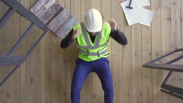 Happy builder in de helm en groene jas liggend op de vloer opzoeken. Hamer en tekeningen die naast hem liggen. De man rust na het werk. Top View. — Stockvideo