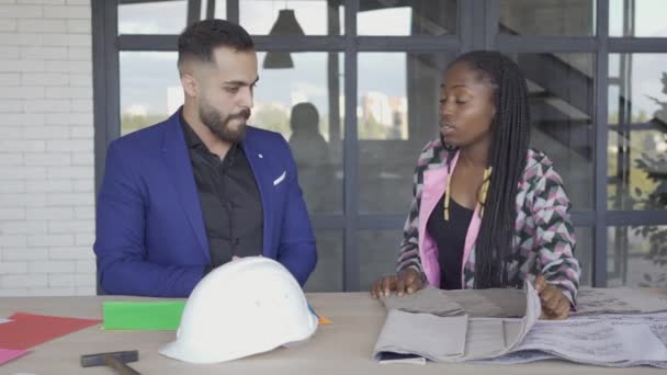 Pareja multicultural eligiendo tapicería y estilo de muebles. Hombre caucásico y mujer afroamericana decorando su casa. Diseño de interiores . — Vídeos de Stock