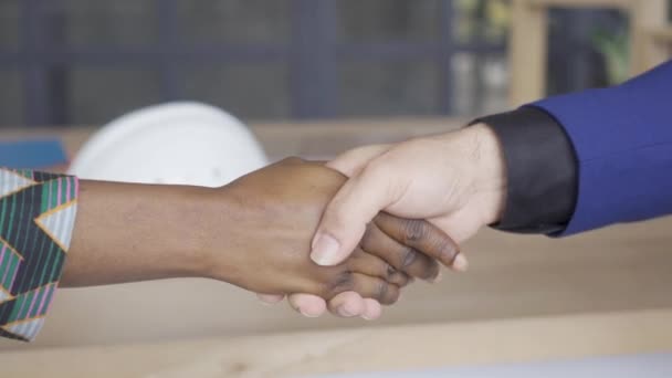 白人男性とアフリカ系アメリカ人の女性がテーブルの前で握手をする。デザイナーと顧客の契約書. — ストック動画