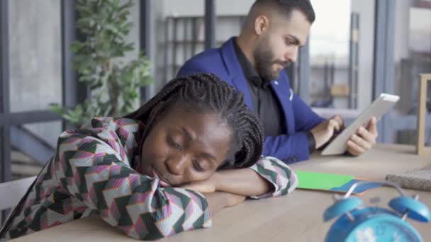 Femme afro-américaine sieste en attendant le concepteur masculin caucasien pour faire le projet sur sa tablette . — Video