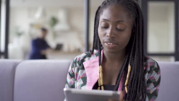 Молоді досить афро-американської жінки з проблемою шкіри сидять на дому, працюючи з її планшетом. Дозвілля в приміщенні. Дівчина відпочиває після роботи. Гаджет наркоманії — стокове відео