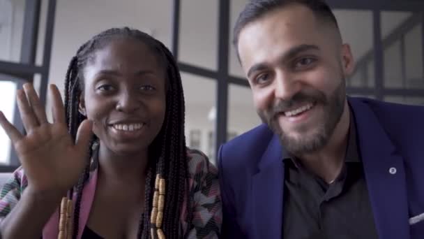 Primer plano de pareja multirracial sonriendo a la cámara y saludando. Caucásico hombre y mujer afroamericana hablando con sus amigos o familiares mediante chat de vídeo . — Vídeos de Stock