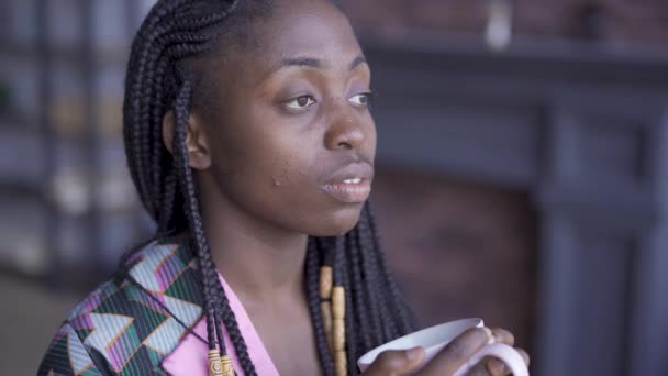 Närbild porträtt av tankeväckande ung afrikansk amerikansk kvinna med afro Pigtails titta bort dricka kaffe. Flickan med problem hud vilar hemma. Hudvårdskoncept — Stockvideo