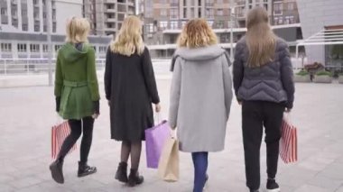 Geri görünümü güzel kız sokakta mutlu bir şekilde konuşurken yürüyor. Şehirde yürüyen alışveriş poşetleri olan dört moda kadını. Birlikte boş zaman. Kızlar kendi alımları zevk