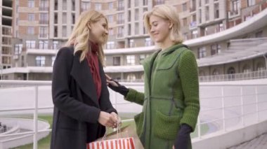 İki güzel sarışın kız birbirlerine alışveriş çantaları gösteren sokakta duruyor. İki moda kadını alışverişlerini sergiliyor. Kaygısız yaşam tarzı. Alışverişakolik