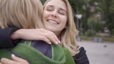 İki beyaz kız arkadaş birbirlerine sarılıyor, birbirlerini gördüklerine sevinmiş. Kadınlar sokakta buluştu. Toplantının samimi sevinci. Omzundan ateş ediyor. Dostane ilişki