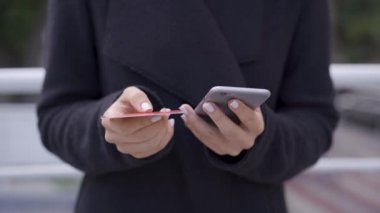 Siyah ceketli genç kadının cep telefonu ve kredi kartıyla internetüzerinden ödeme yapması. Kolay ödeme, modern teknoloji