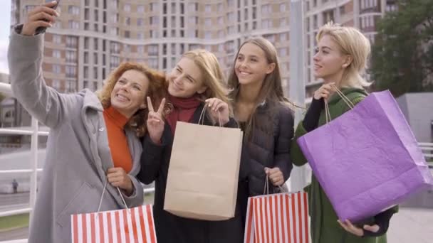 Quatro lindas namoradas posando na rua enquanto uma delas toma selfie. Quatro mulheres da moda com sacos de compras na cidade. Lazer juntos. Meninas gostando de suas compras. Shopaholismo — Vídeo de Stock