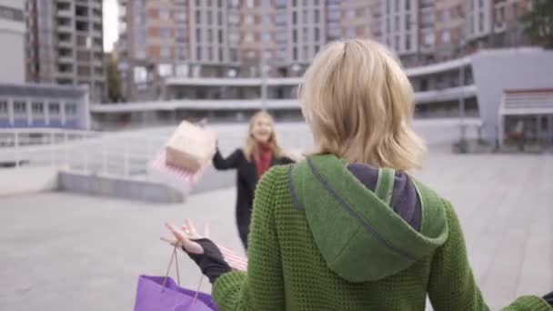 Δύο ξανθιές φιλενάδες με σακούλες για ψώνια συναντήθηκαν στο δρόμο μετά τα ψώνια. Δύο γυναίκες της μόδας αγκαλιάζονται, χαίρονται που βλέπουν ο ένας τον άλλον. Ανέμελη ζωή. Αγορανατισμός — Αρχείο Βίντεο