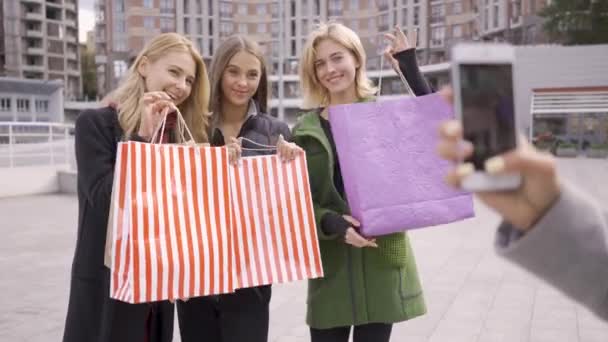 Mujer caucásica tomando fotos de sus tres amigos con bolsas de compras. Cuatro mujeres de moda descansando después de ir de compras. Chicas disfrutando de sus compras. Shopaholism . — Vídeo de stock
