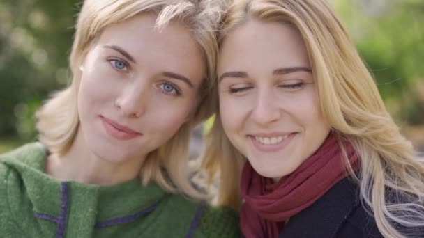 Twee mooie blonde Kaukasische meisjes kijken naar camera en glimlachend. Vriendelijke relatie. Jonge vrouwen tijd samen doorbrengen buiten. — Stockvideo