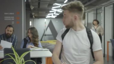 Beyaz tişörtlü konsantre genç adam modern ofiste masada dizüstü bilgisayarla çalışıyor. anager işi bitirdi. Işyeri.
