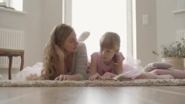 Mutlu sarışın beyaz anne ve küçük kızı evde kabarık halı üzerinde katta yatıyordu. Kitap okuyan kız. Çocuk eğitimi. Annelik, çocukluk, bir ebeveyn kavramı. Mutlu aile
