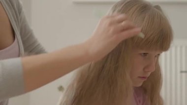 Sevimli sarışın kızını tarayan genç kadının yakın elleri. Annelik kavramı, çocukluk. İçeride boş zaman. Mutlu aile.