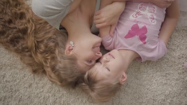 幸福的白种人母亲和她的小女儿躺在蓬松的地毯在家里的顶视图。女人和女孩在家休息，面带微笑。幸福的家庭. — 图库视频影像