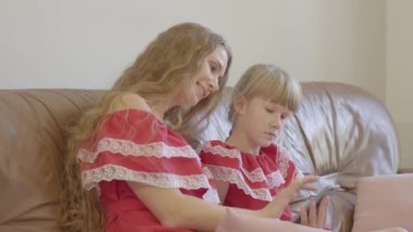 Mutlu sarışın beyaz anne ve aynı elbiseler içinde küçük kızı evde cep telefonu kullanarak kanepede oturan. Annelik, çocukluk, bir ebeveyn kavramı. Mutlu aile