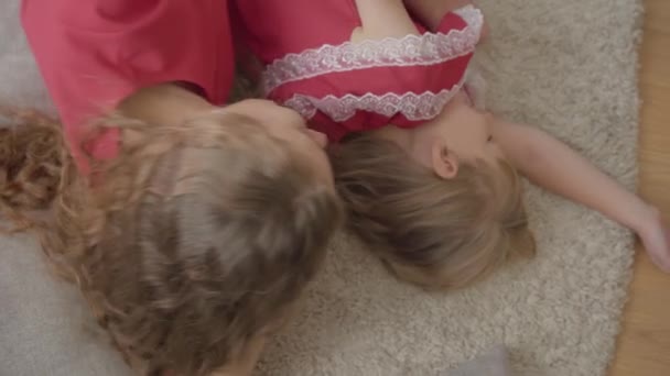 Draufsicht auf eine glückliche Mutter und ihre Tochter in den gleichen roten Kleidern, die auf dem flauschigen Teppich liegen. Frau und Mädchen ruhen sich am Wochenende zu Hause aus. glückliche Familie. — Stockvideo
