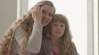 Gülümseyen genç kadın kameraya bakıyor ve uykulu küçük kıza sarılıyor. Cucasian anne sevimli bir sarışın kızı ile vakit geçirmek.