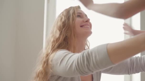 Klein meisje met lang krullend blond haar knuffelen aantrekkelijk jonge blanke vrouw. Dochter toont haar liefde aan de moeder. — Stockvideo